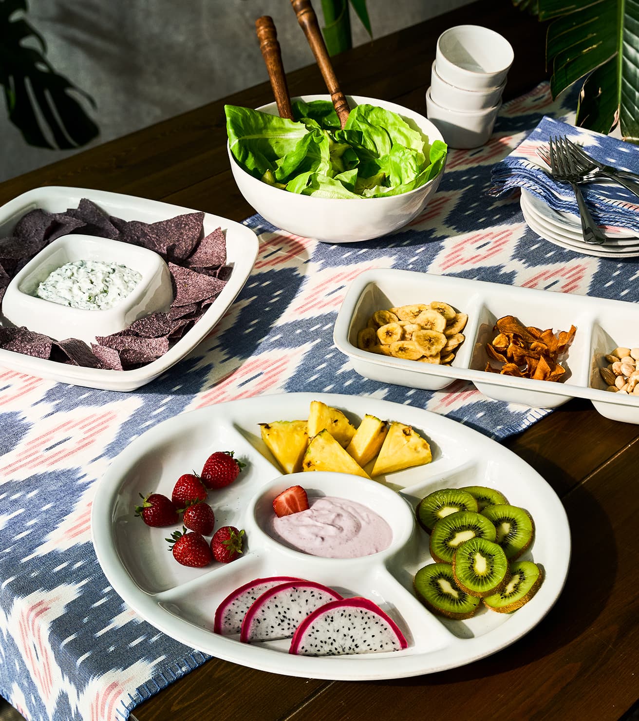 Assorted snacks including chips, salad, and fruits on a table with a patterned tablecloth.