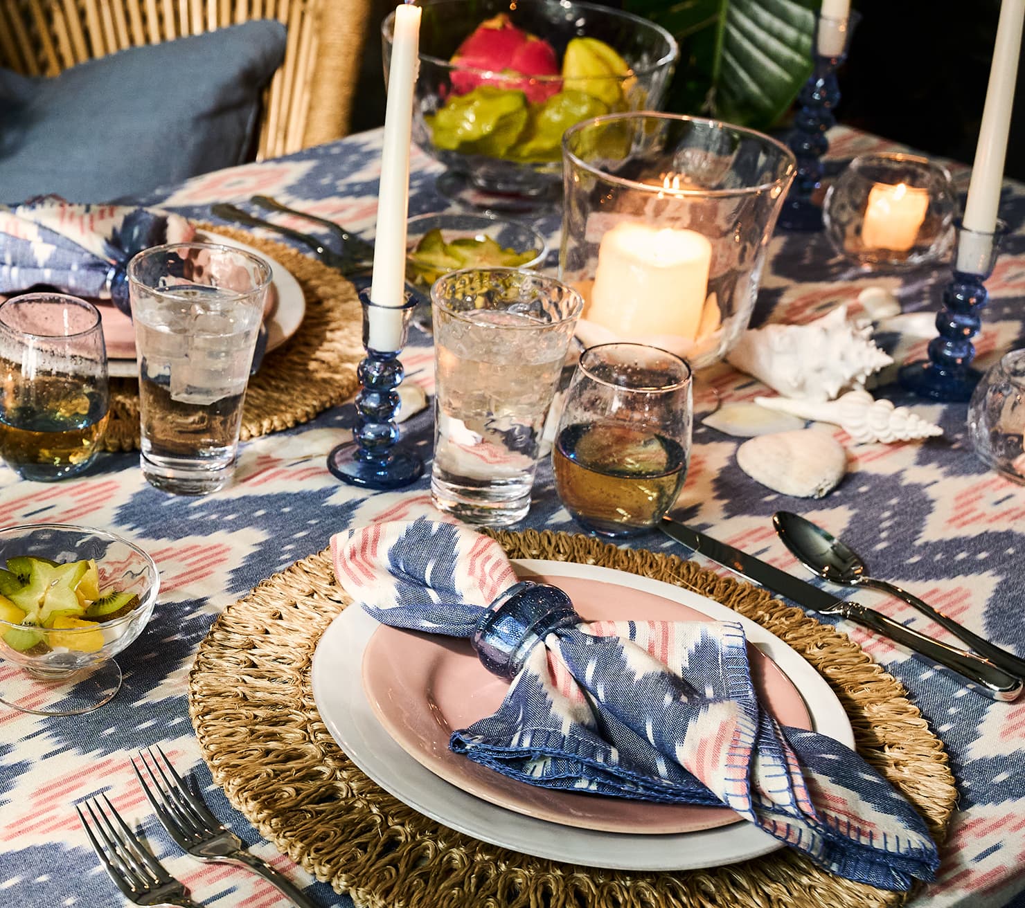 Dining table setting with plates, glasses, and candles on a patterned tablecloth.