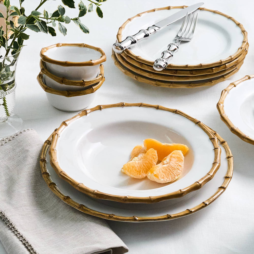 Dinnerware set with bamboo-like rim on a table with fruit and cutlery.