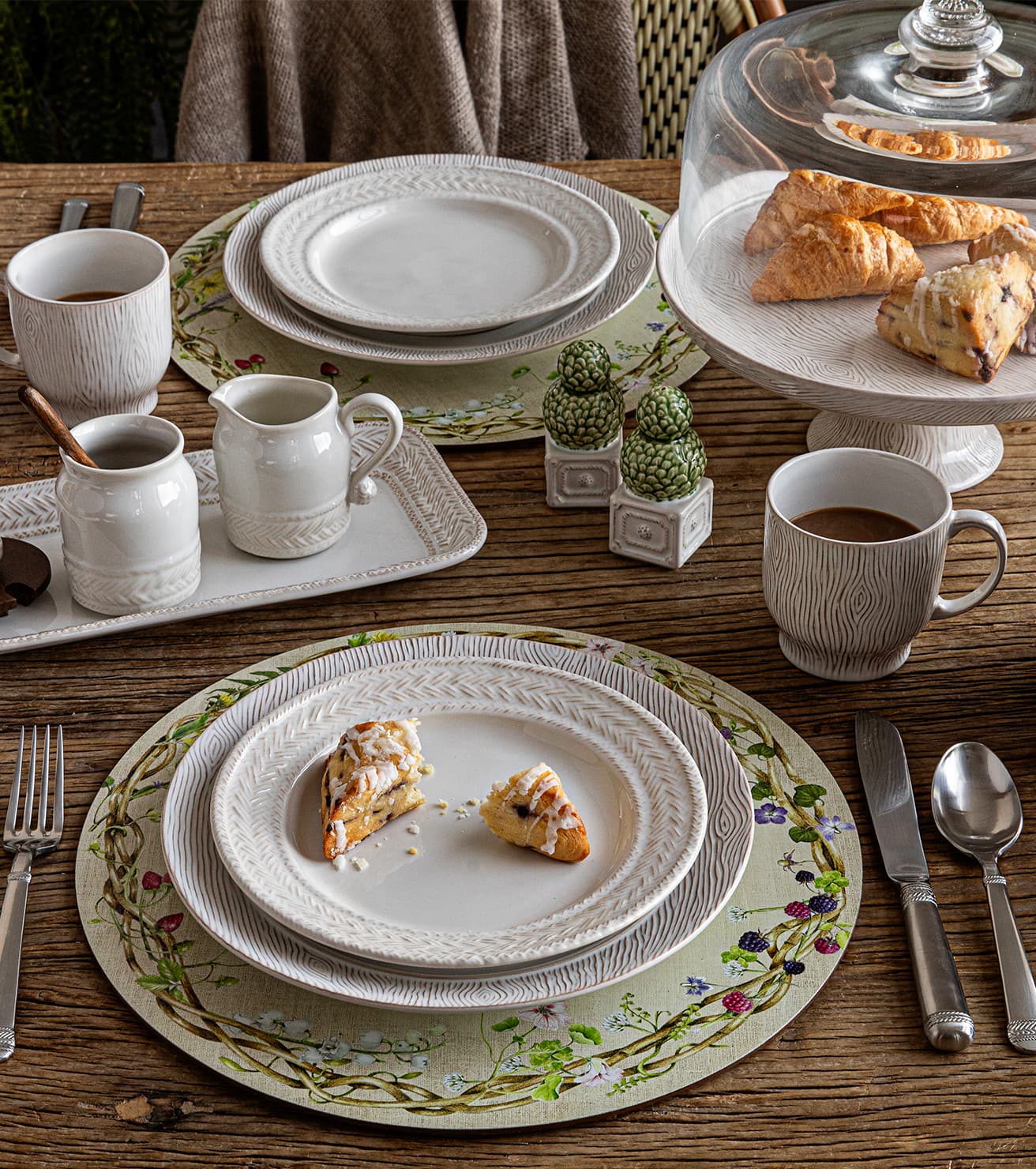 Dining table setting with plates, cups, and pastries on a wooden surface.