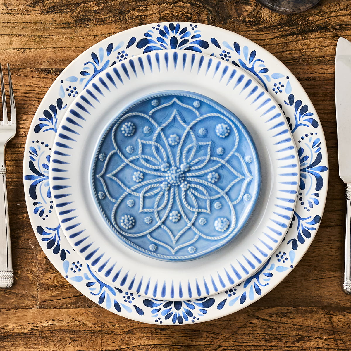 Decorative blue and white plate on a wooden table with cutlery.