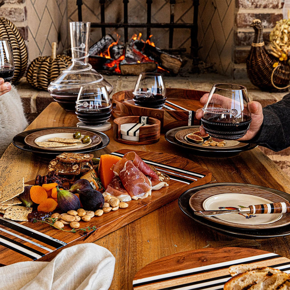 People gather around a wine and cheese plate on a coffee table in front of a fire.