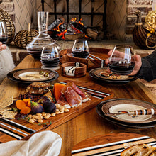 Dining table with wine, charcuterie board, and glasses in front of a fireplace.