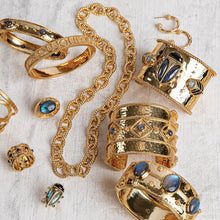 Gold and blue labradorite bracelets, cuffs, rings and earrings are placed on a white linen cloth.