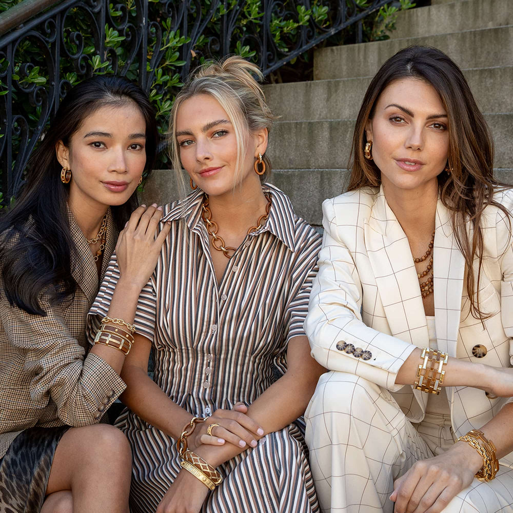 Three women sitting on steps wearing stylish outfits and accessories.