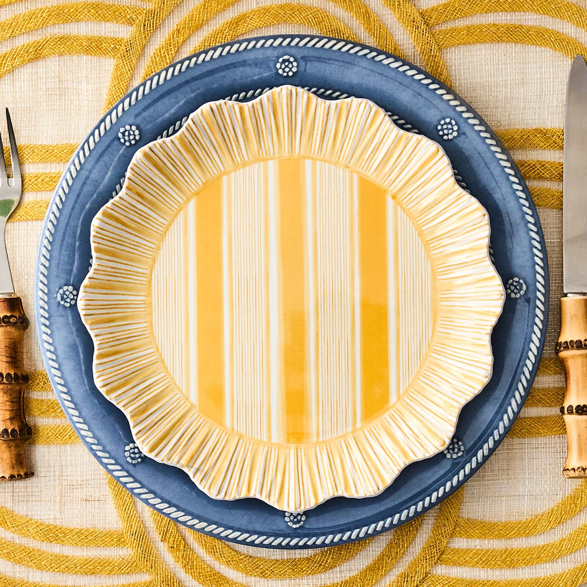 Decorative plate with blue rim and yellow center on a striped tablecloth