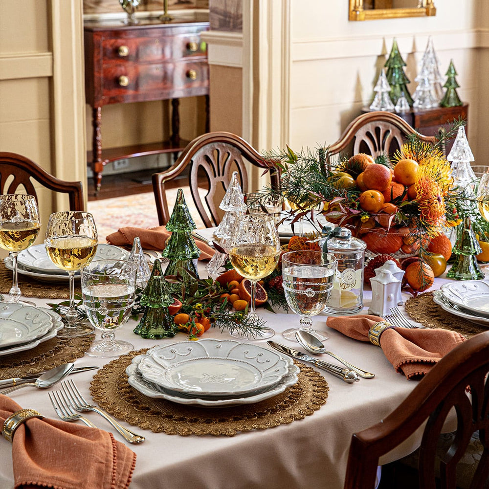 Jardins du Monde place setting sits on the top of a gold placemat with glass Christmas trees as a centerpiece. 