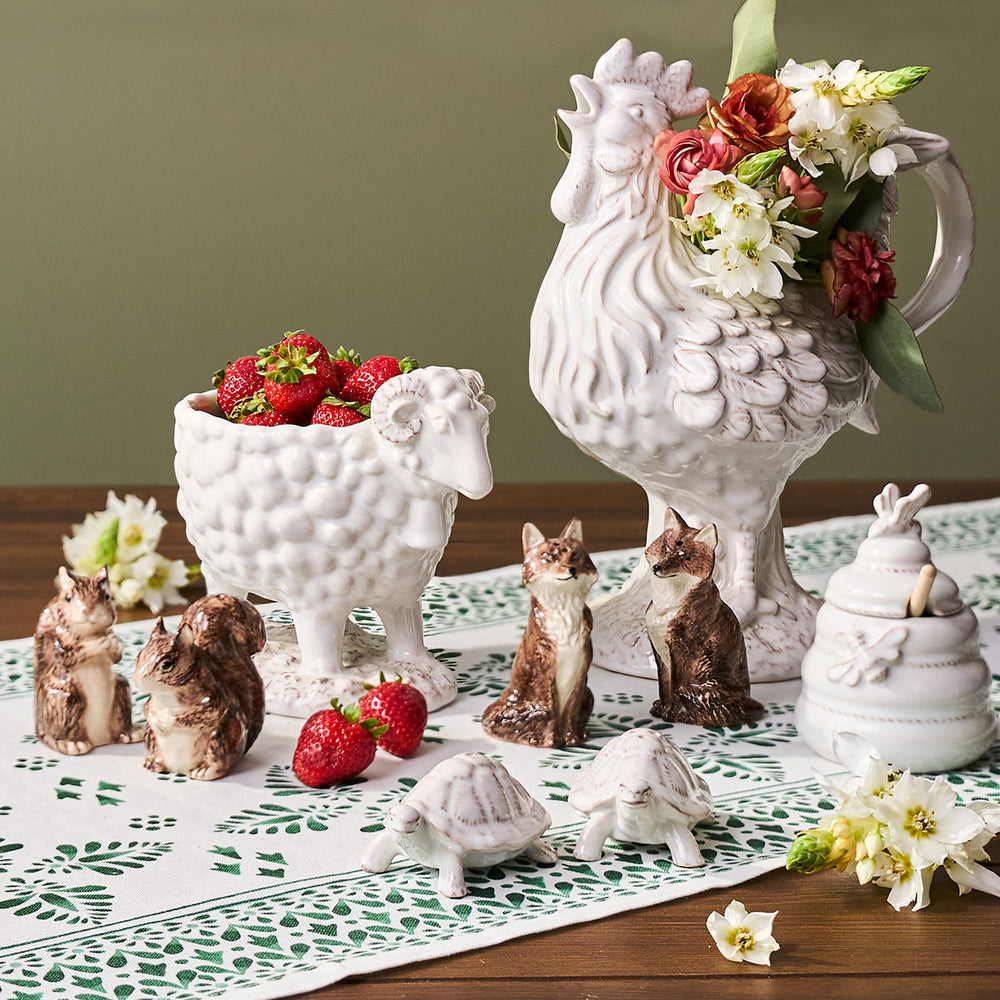 Decorative ceramic rooster with flowers and small animal figurines on a table.