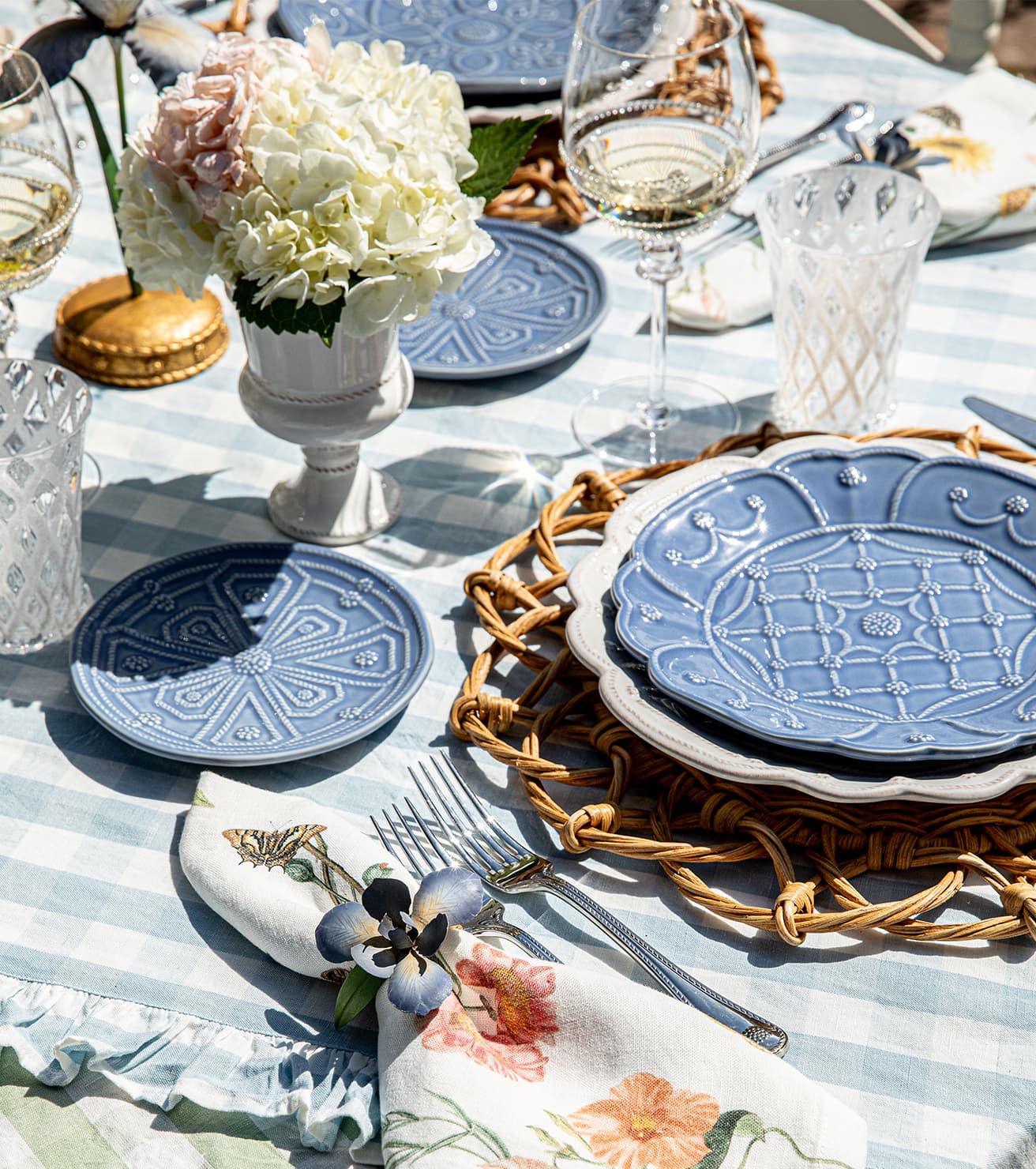 Elegant table setting with blue plates, floral centerpieces, and striped tablecloth.