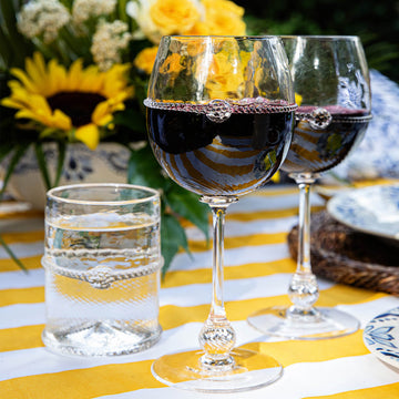 Deep red white glasses and water sit atop a bright yellow and white striped tablecloth. Matching sunflowers bloom behind them.