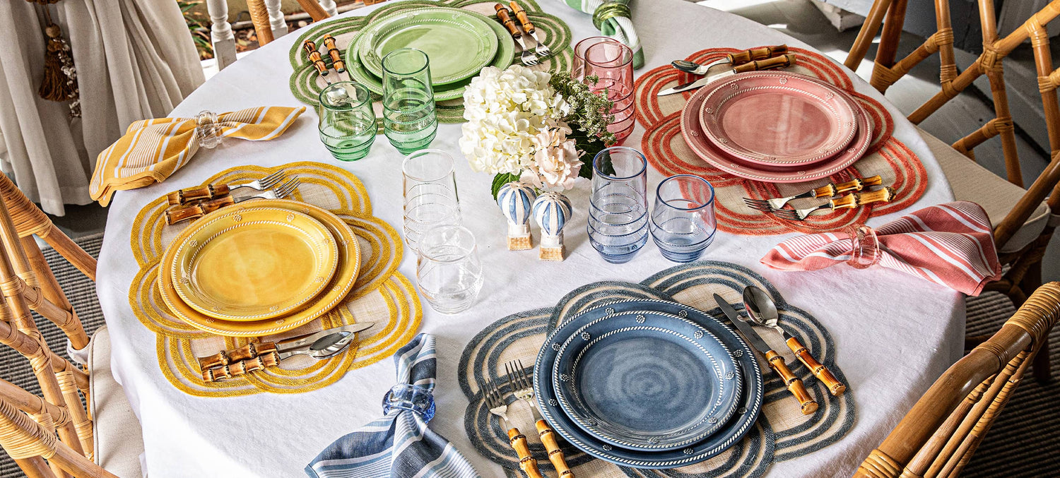 Dining table set with colorful plates, glasses, and cutlery on a white tablecloth.