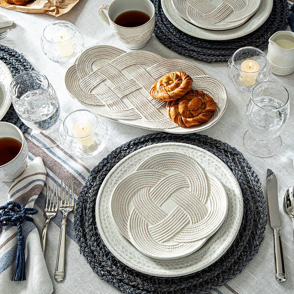 Elegant table setting with woven placemats and plates, candles, and pastries.