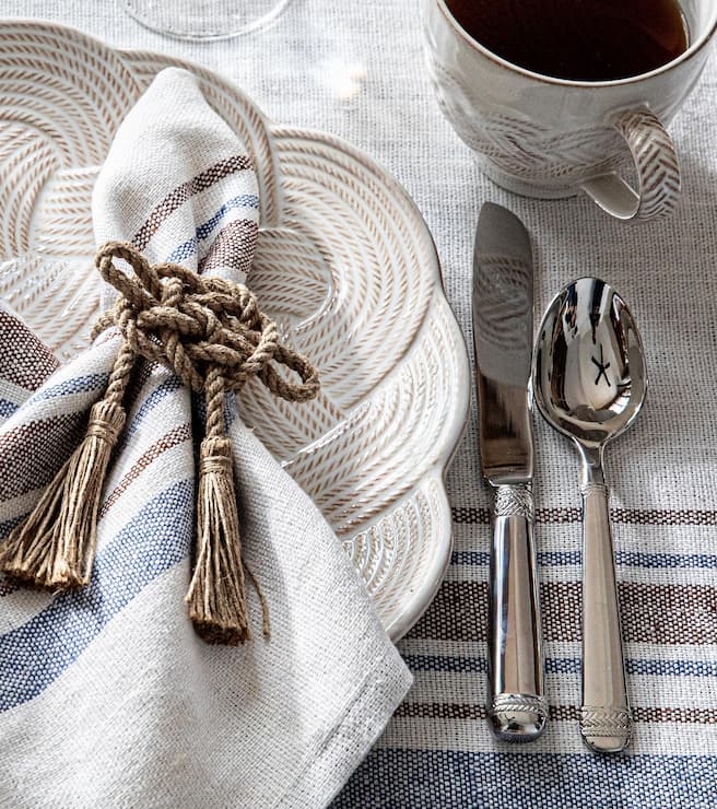 Table setting with a cup, plate, and cutlery on a striped tablecloth.