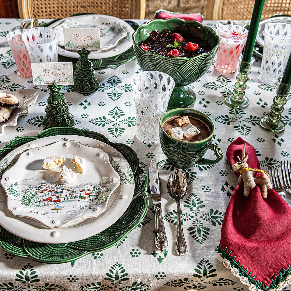 Decorative Christmas table setting with green and white patterned tablecloth, festive North Pole plates, and red napkin.