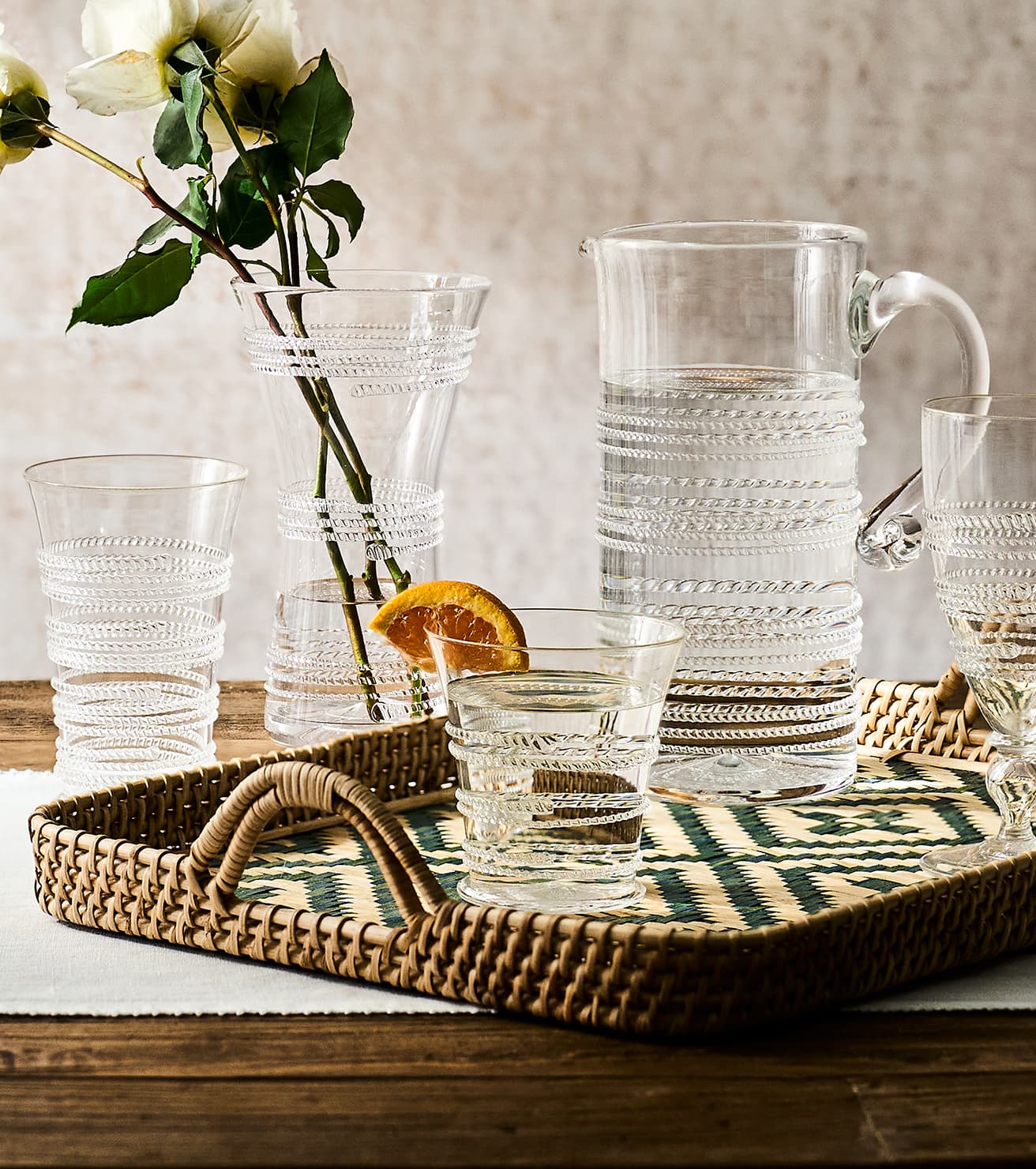 Clear glassware set on a woven tray with a neutral background