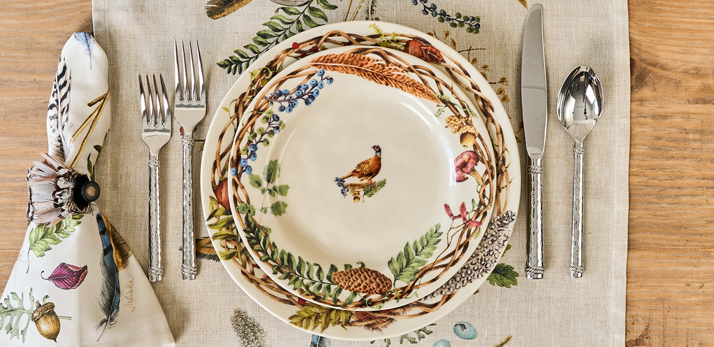 Decorative table setting with a plate featuring bird illustrations, accompanied by cutlery and a napkin.