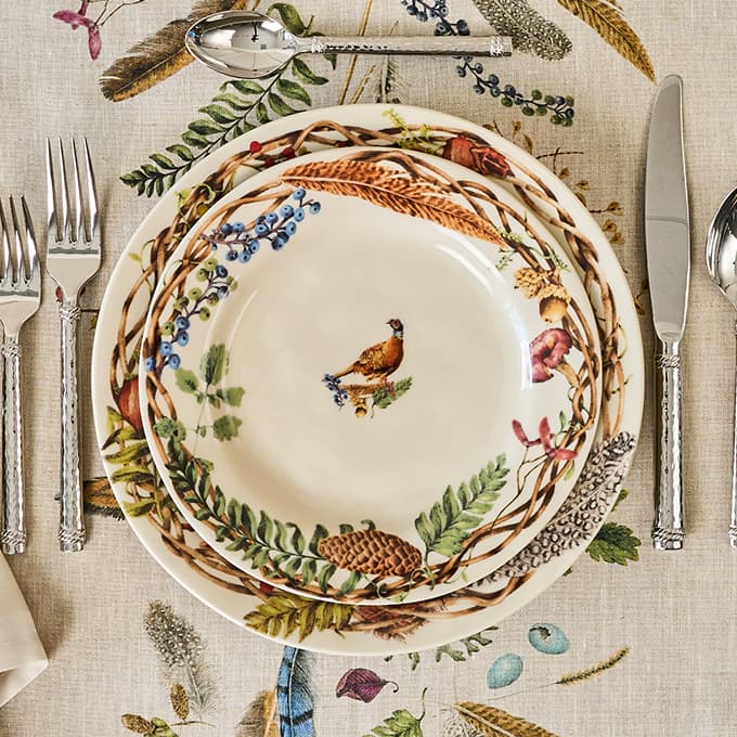 Decorative plate with nature-themed design on a table setting with cutlery.