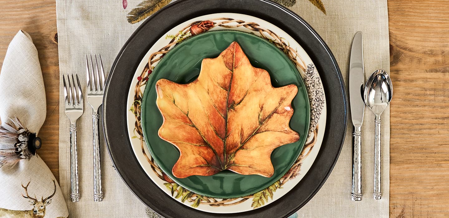Decorative plate with leaf design on a table setting with cutlery and napkin.
