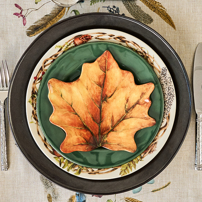 Decorative plate with a large leaf on a patterned tablecloth