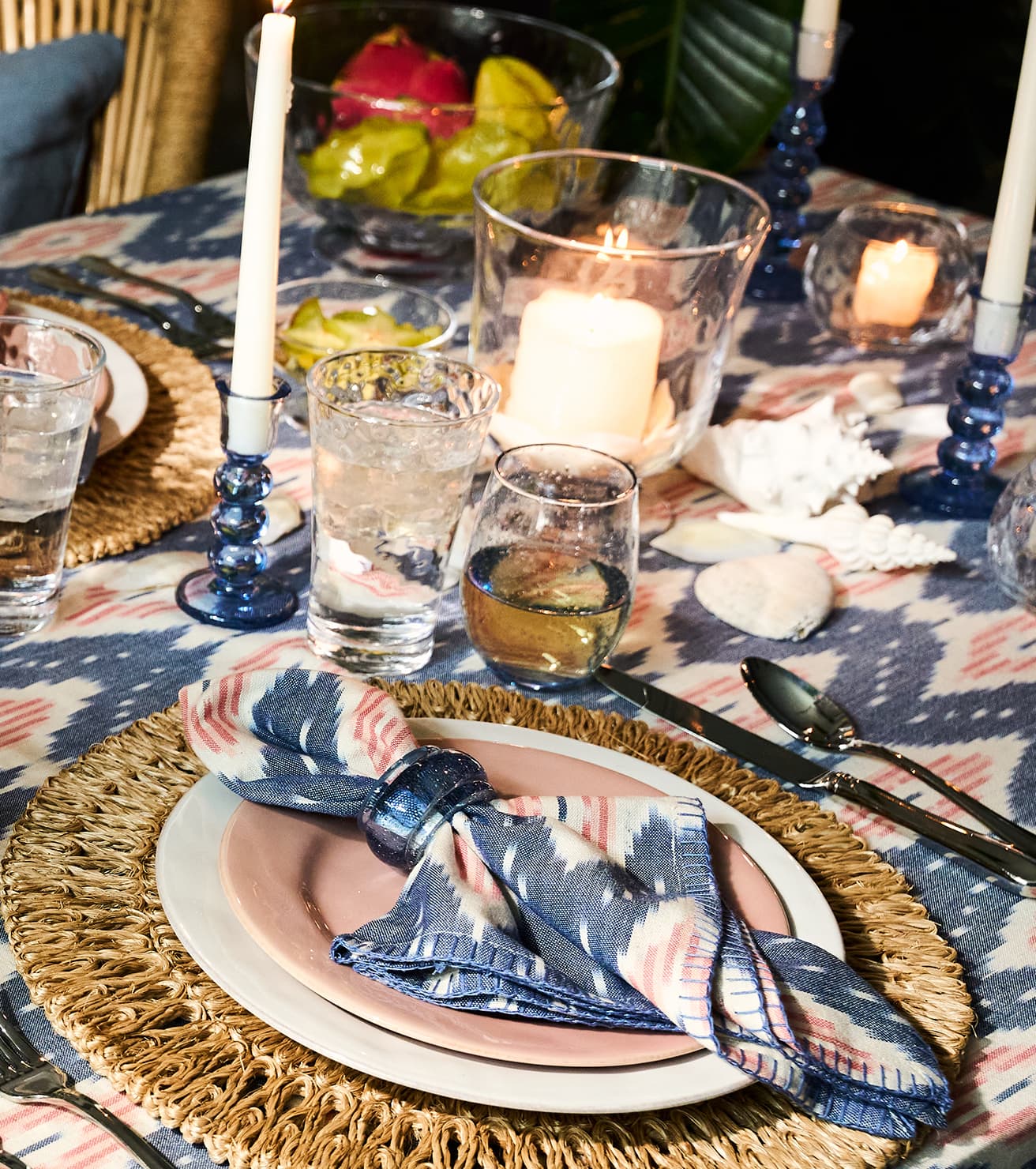 Dining table setting with plates, glasses, and candles on a patterned tablecloth.