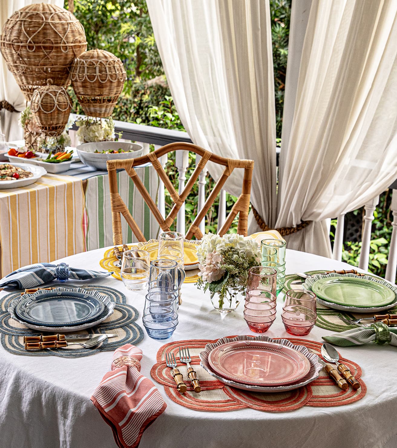 Dining table set with plates, glasses, and cutlery on a white tablecloth with a chair and outdoor setting.