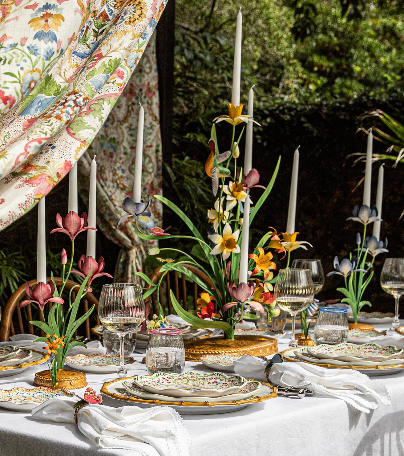 Elegant outdoor table setting with floral centerpieces, candles, and fine china.