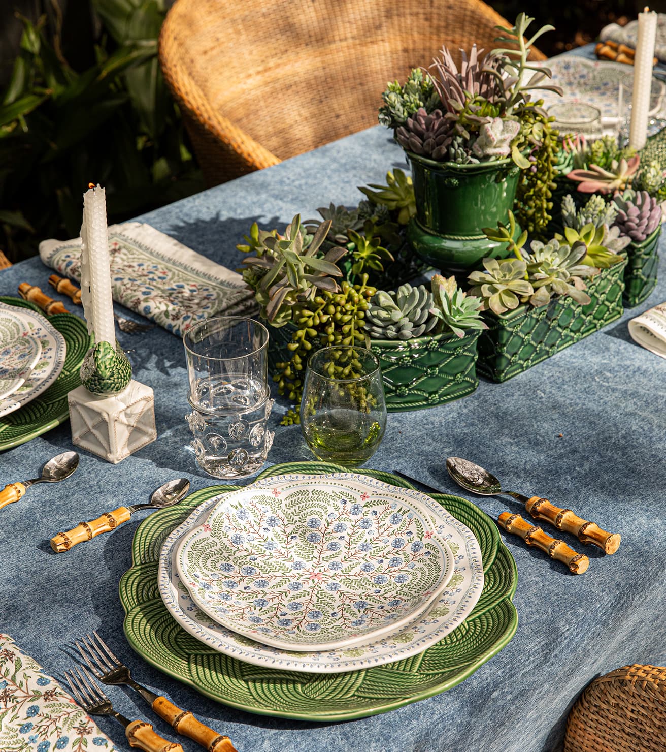 Decorative table setting with green plates, silverware, and plants on a blue tablecloth.