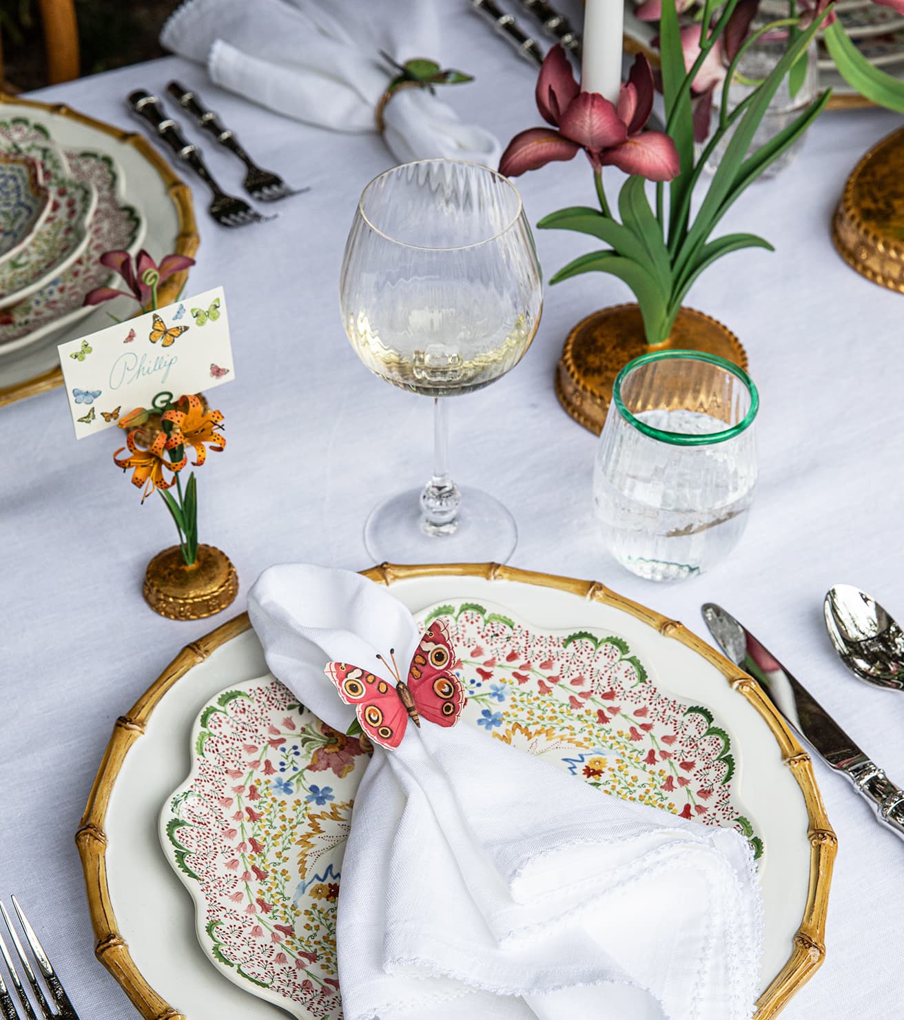 Decorative table setting with floral plates, napkins, and glasses on a white tablecloth.