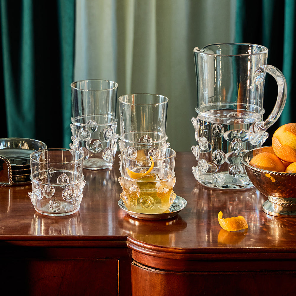 Set of glass tumblers and a pitcher on a wooden table with oranges.