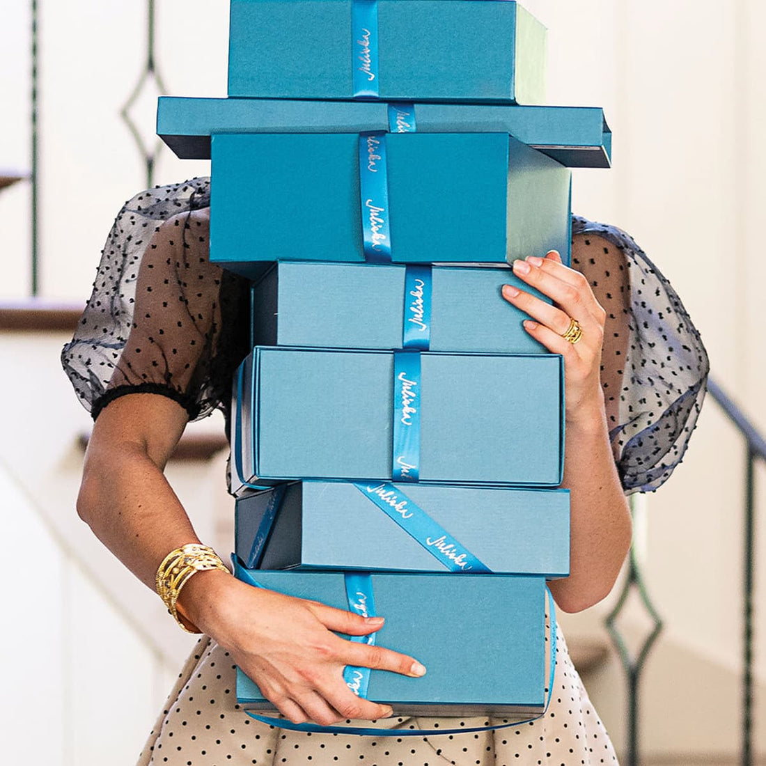 Person holding a stack of blue gift boxes with ribbons