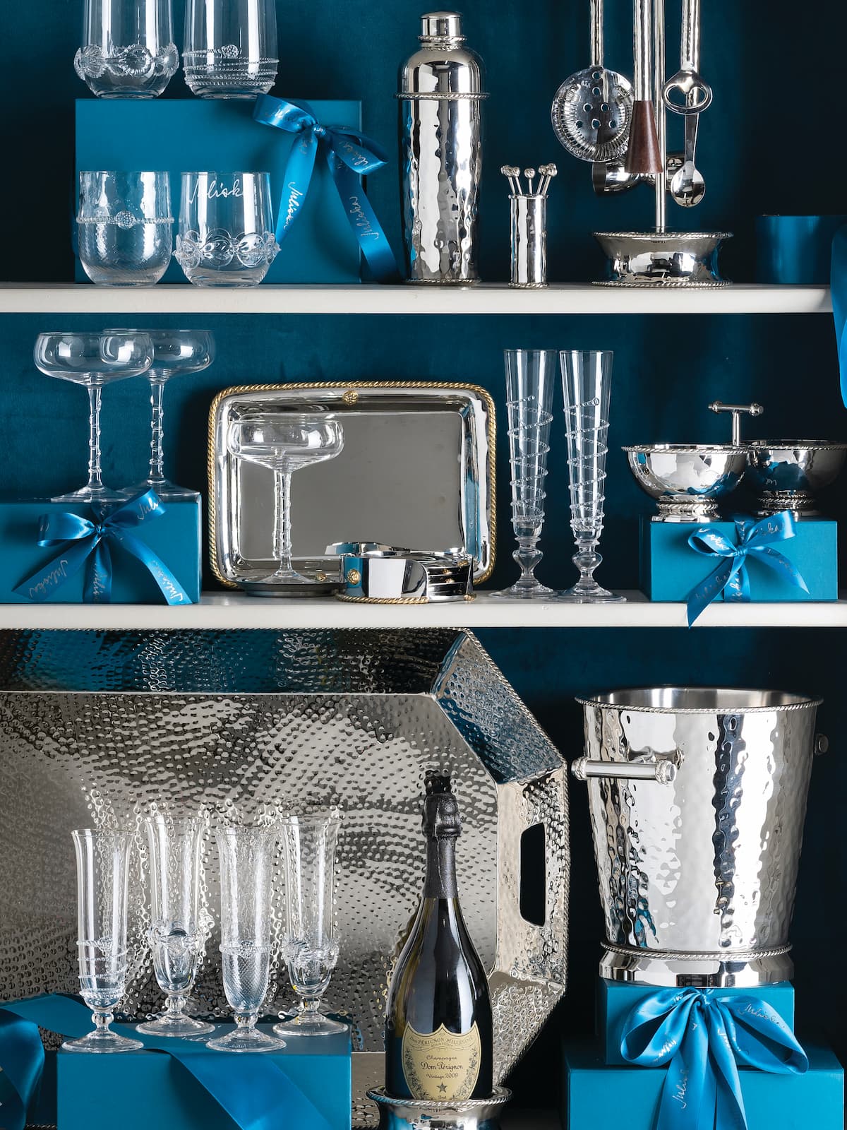 Shelves with silver barware, glasses, and blue gift boxes against a dark background