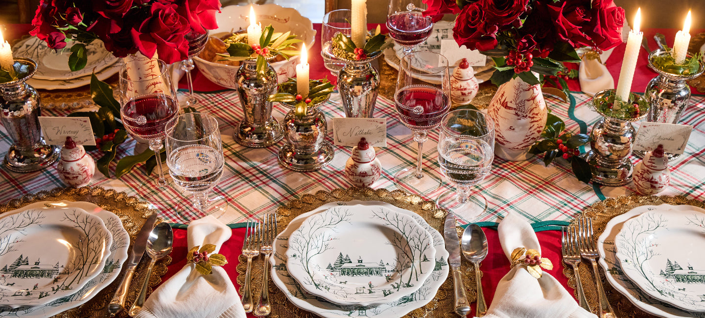 Elegant Christmas table setting with red and green decorations, candles, and plaid tablecloth.