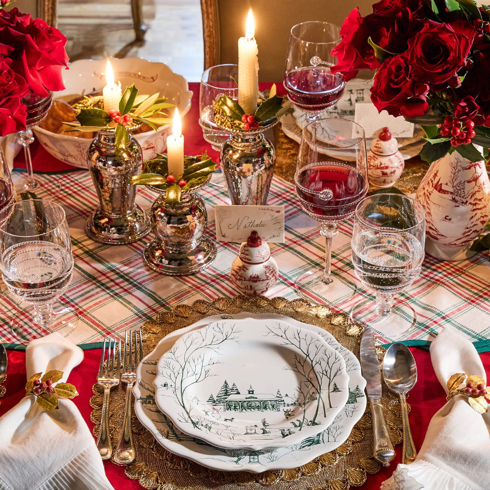 Elegant Christmas dinner table setting with red and green decorations, candles, and patterned tablecloth.