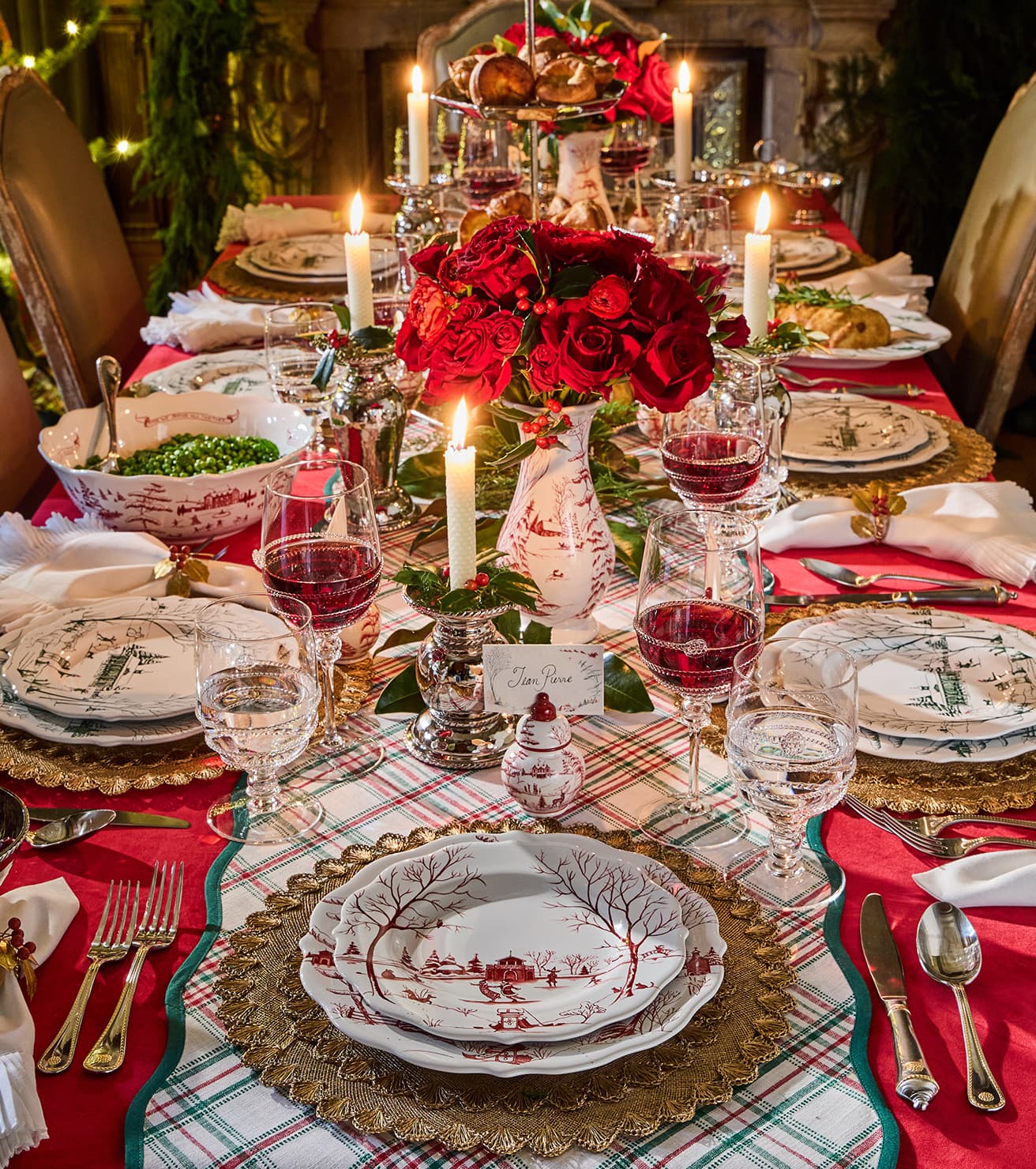 Decorative Christmas table setting with red and white theme, candles, and floral centerpieces.