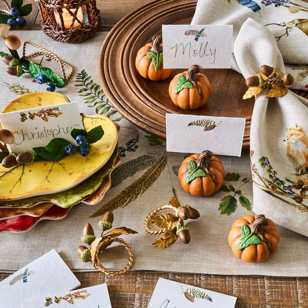 Thanksgiving table setting with pumpkins, place cards, and decorative napkins.