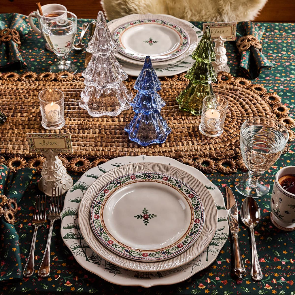 Decorative table setting with patterned plates, cutlery, and candles on a textured tablecloth.