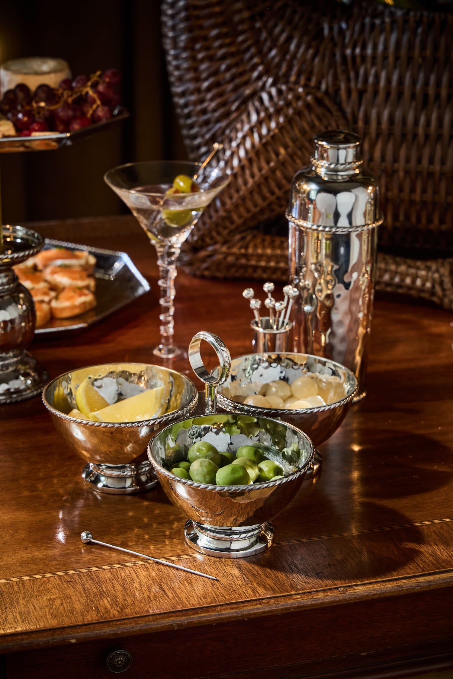 Bar setup with cocktail shaker, glasses, and garnishes on a wooden surface.