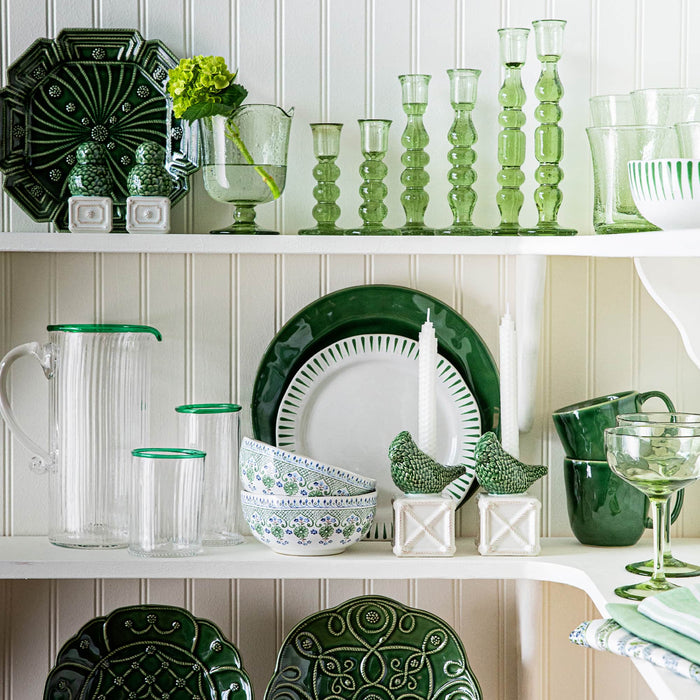 Green and white ceramic dishes and glassware on a white shelf against a white paneled wall.