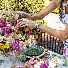 Woman fixing a floral display on an outdoor table. The woman is wearing Capucine De Wulf bracelets and ring
