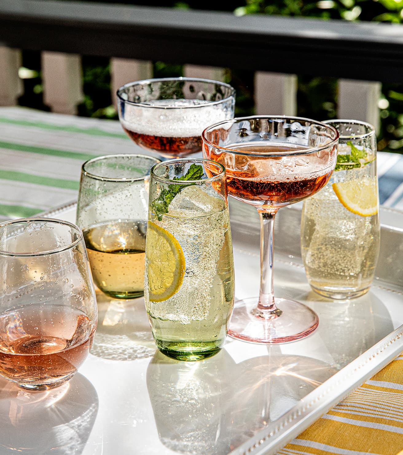Assorted glasses of drinks including wine, champagne, and water with lemon slices on a table outdoors.