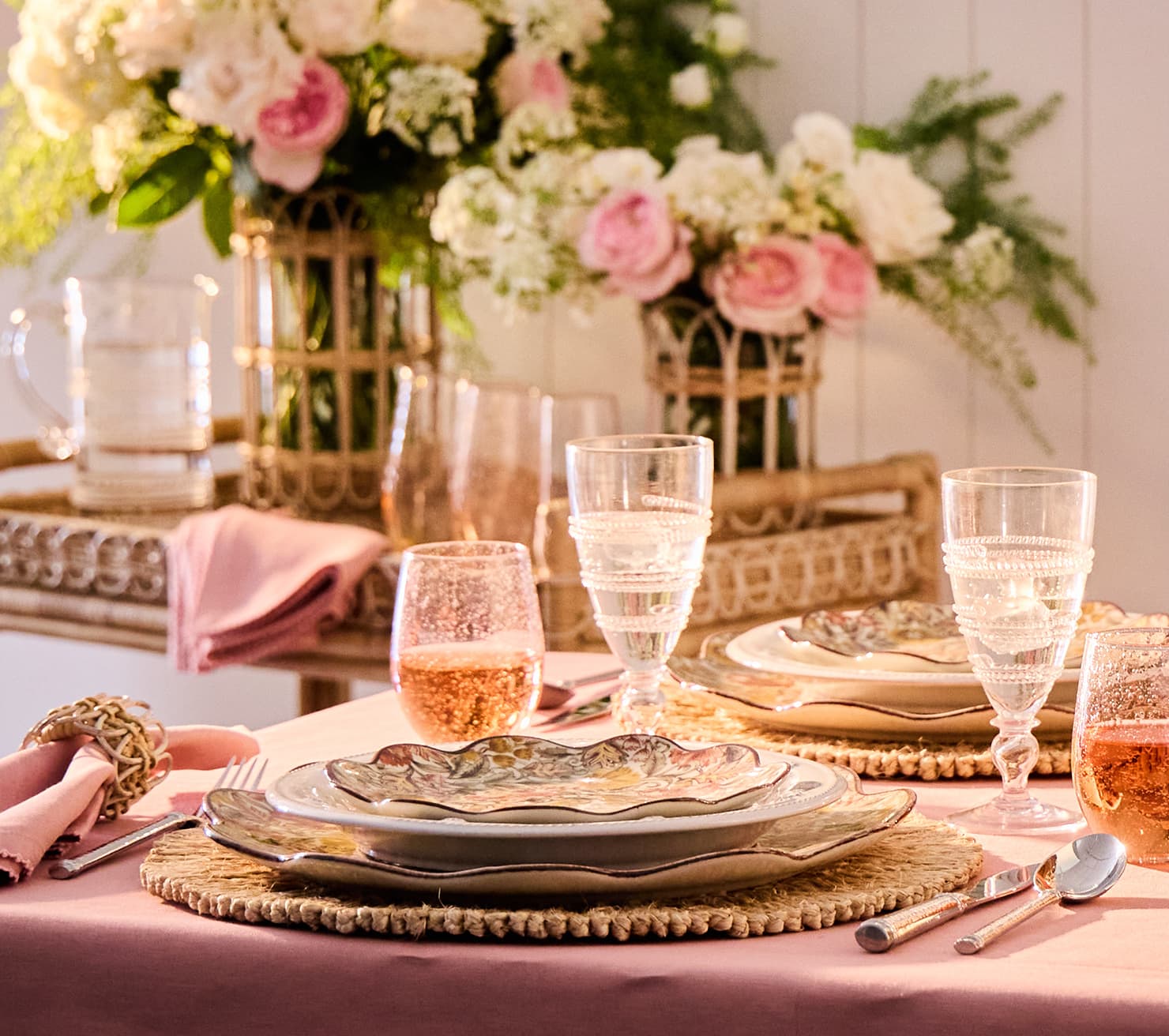 Elegant table setting with floral centerpiece, glassware, and cutlery on a pink tablecloth.