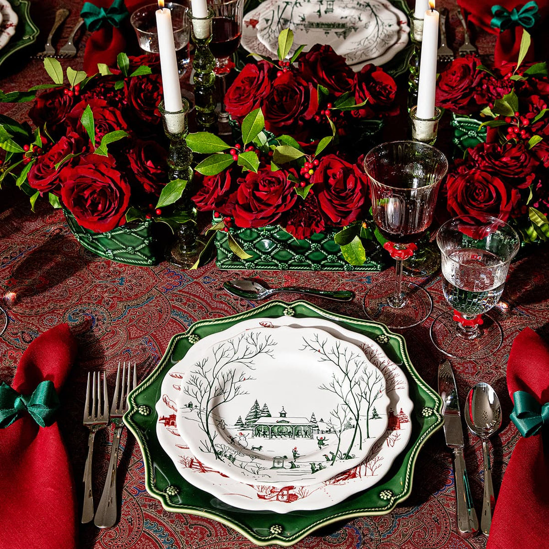 Tablesetting with a red paisley tablecloth, green Berry & Thread Charger plate and Country Estate Winter Frolic Dinner and Salad plate. Large floral display of red roses in a green planter are the centerpiece.