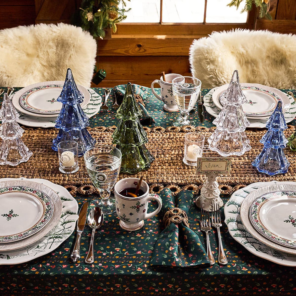 Set dining table with Christmas decorations, including glass trees and patterned plates.