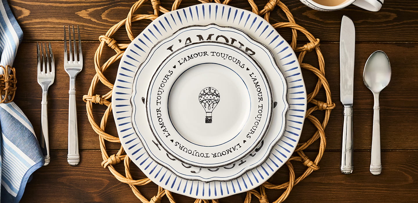 Table setting with a decorative plate, cutlery, and napkin on a wooden surface.