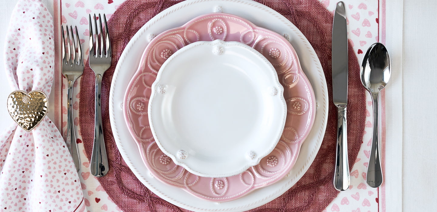 Dining table setting with pink plates, silverware, and a heart-shaped napkin holder.