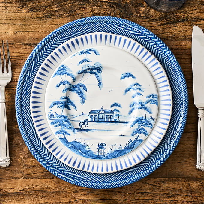 Blue and white decorative plate with landscape design on a wooden table with cutlery.