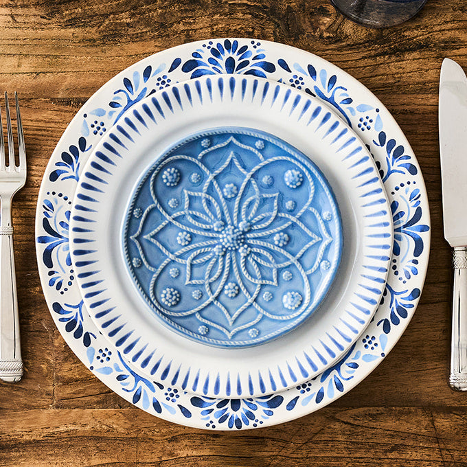 Decorative blue and white plate on a wooden table with cutlery.