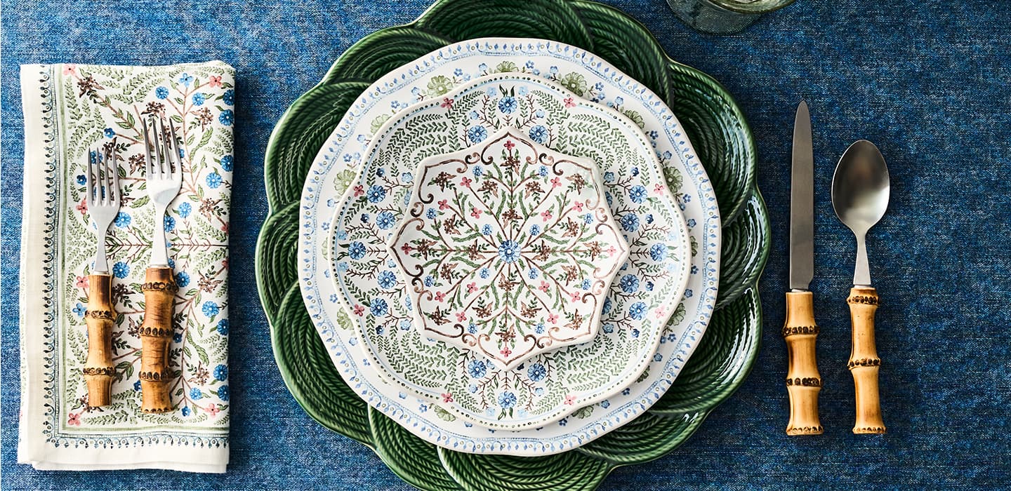Decorative table setting with a patterned plate, green charger, and cutlery on a blue textured surface.