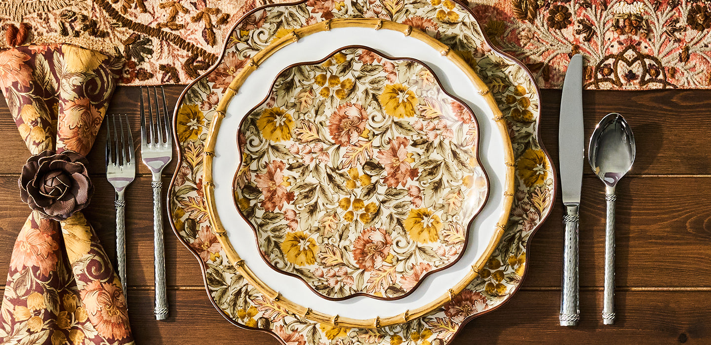 Decorative plate with floral pattern on a wooden table with cutlery and napkins.