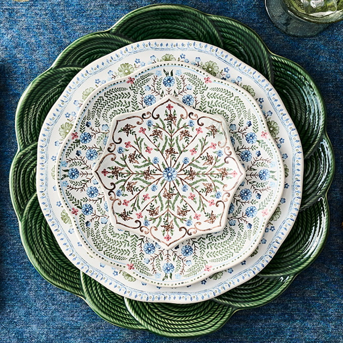 Decorative table setting with a patterned plate and a green charger on a blue textured surface.